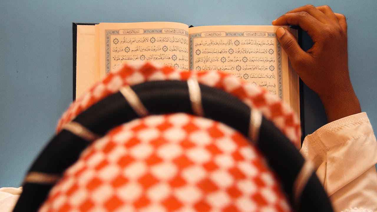 A person in traditional attire reading an open Quran, viewed from above.